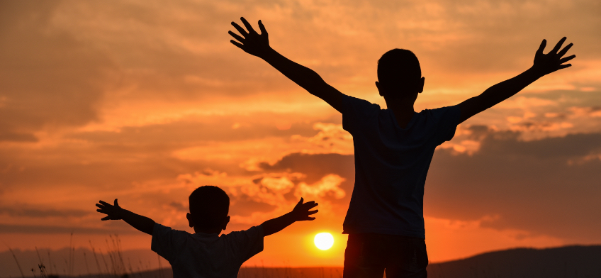 Children with outstretched arms watching the sunset